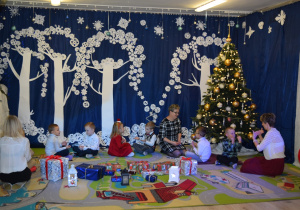 Dzieci z grupy Słoneczka, siedzą na dywanie wśród prezentów i śpiewają piosenkę..